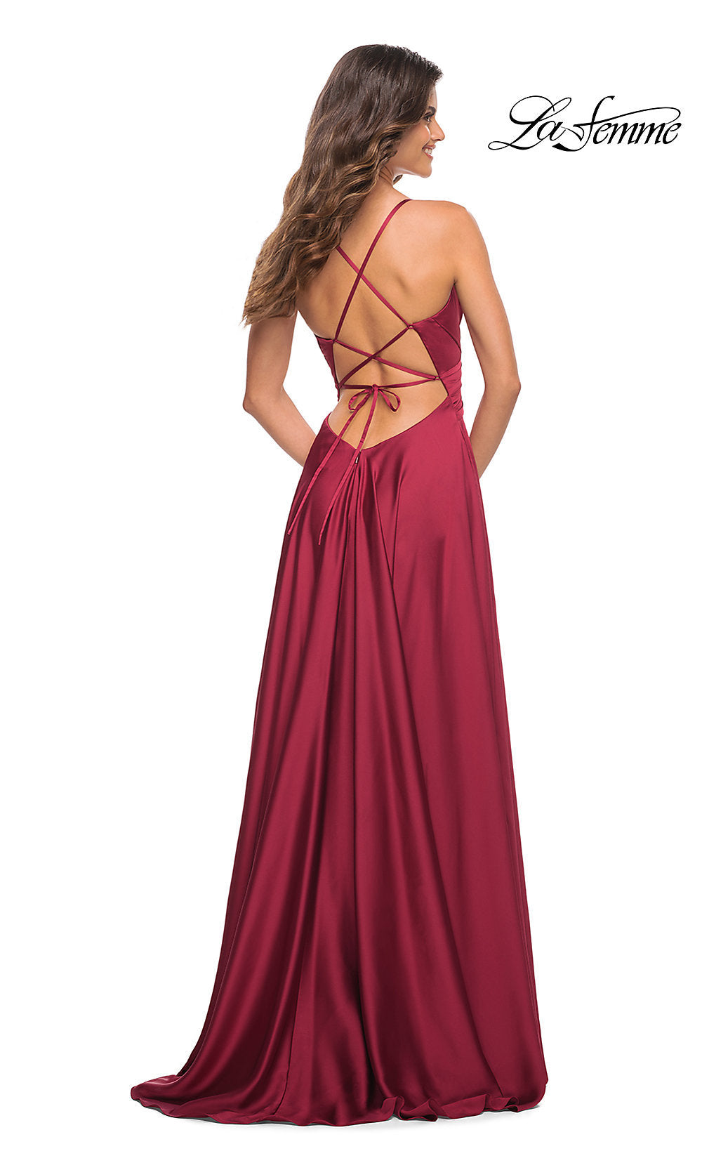 A woman stands facing away, wearing the La Femme Lace-Up Back Long Satin A-Line Prom Dress in deep red. The floor-length gown features a crisscross lace-up open back and tie detail.